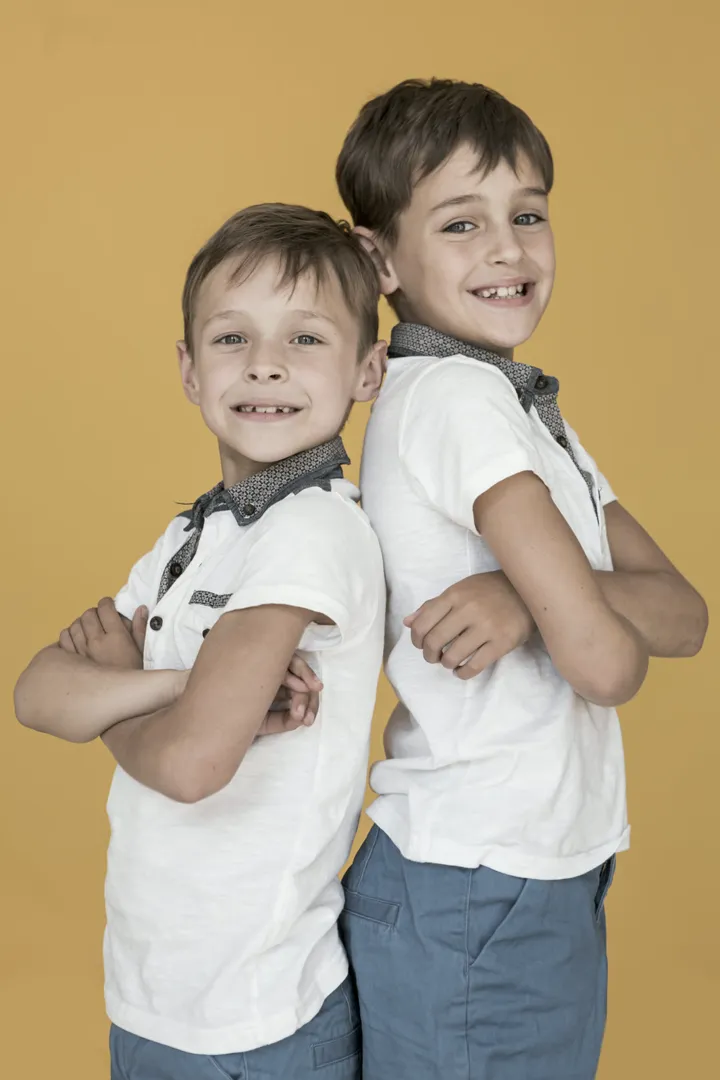 Dois meninos de uniforme, de braços cruzados, sorrindo